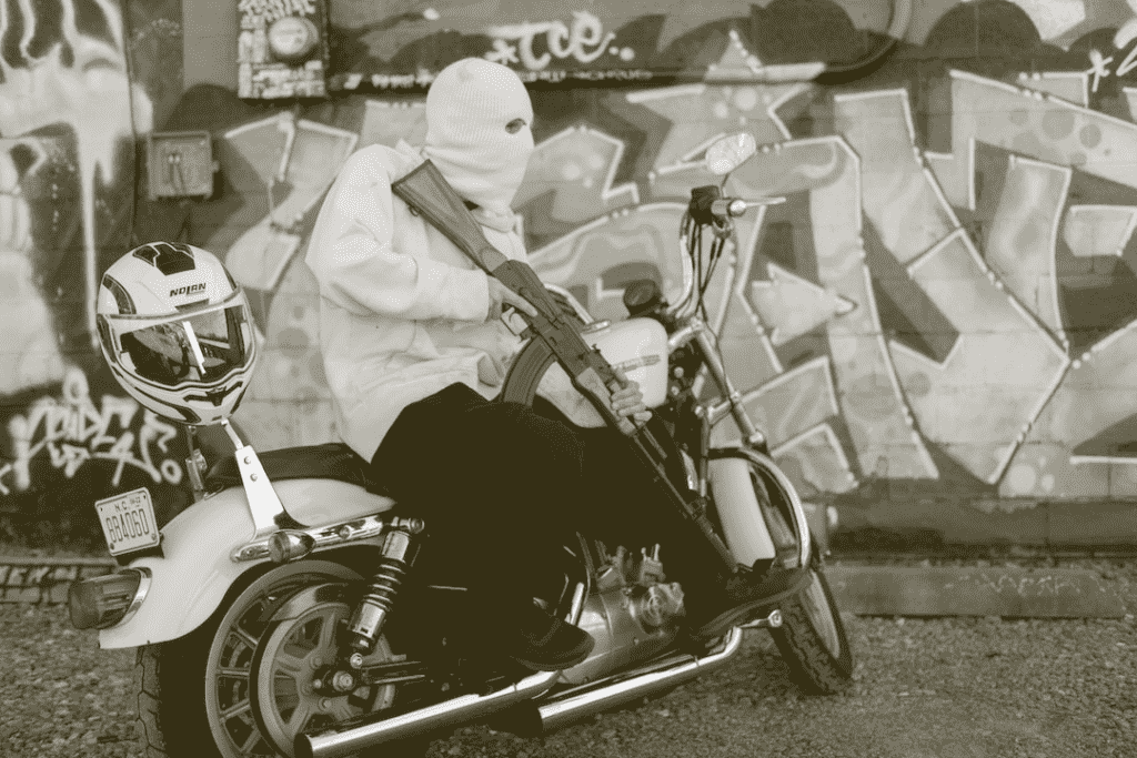 Person with ski mask and large gun on a motorcycle