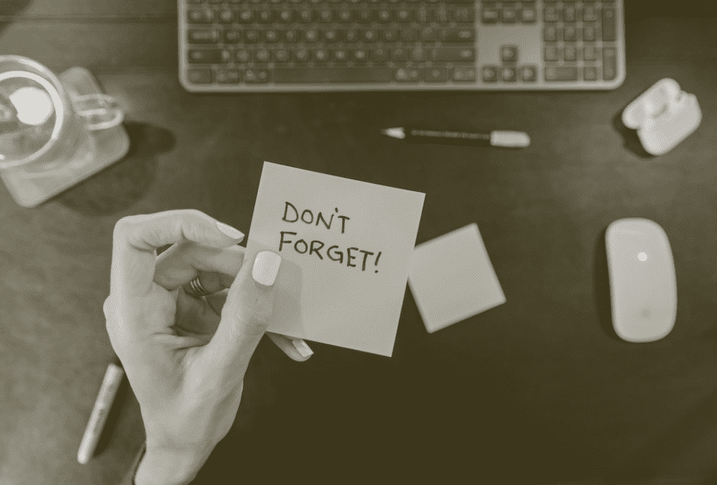 A hand holding up a sticky note that says "DON'T FORGET!"